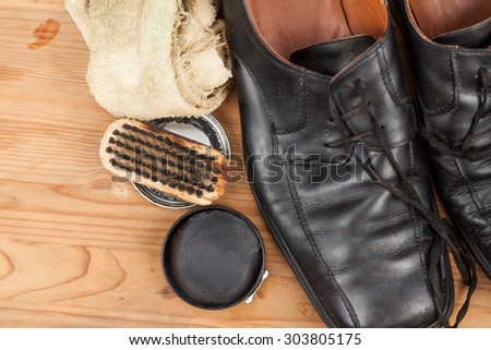 Shoe polish with brush, cloth and worn men shoes on wooden platform.