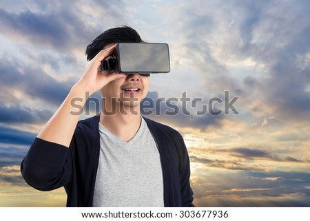 Asian man wearing virtual reality goggle on sky background.