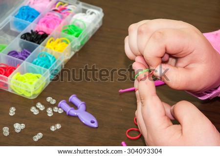 Kids hands creating bracelet with rubber bands and box in the background.