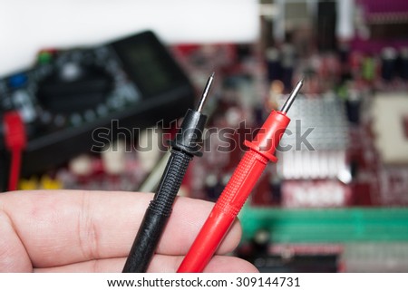 Digital multimeter wires in the service mans hand with printed circuit board in the background.