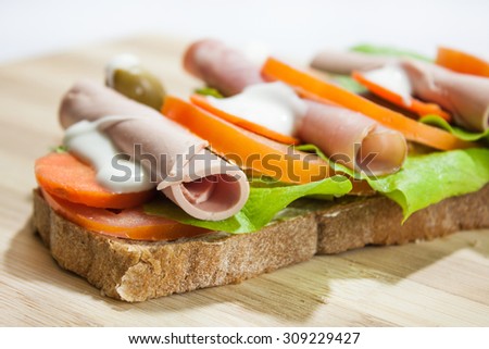 Sandwich on the wooden board. Sandwich with smoked ham, lettuce, olive, carrots and mayonnaise.