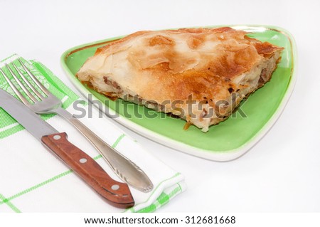 Turkish burek with meat on a green plate with fork and knife.