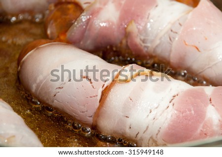 FRYING ROLLED SAUSAGES IN BACON.