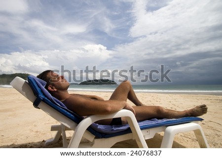 tanned man laid on a chair at a white sand beach, Phuket Island, Thailand