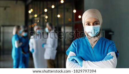 Portrait of Arab woman doctor in hijab, medical mask and gloves standing in hospital. Muslim female medic in traditional headscarf in clinic. Covid-19. Arabian nurse. Coronavirus. Protected.