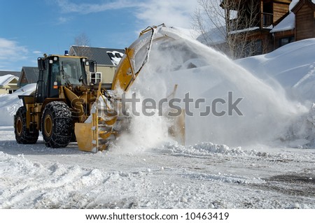 Municipal snow blower clears snow-covered streets producing a plume of snow