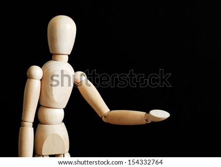 Wooden dummy man present something on black background