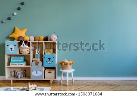 Stylish scandinavian newborn baby room with wooden cabinet, toys, children's chair, natural basket  Modern interior with eucalyptus background walls, wooden parquet and cottona balls. Home decor.