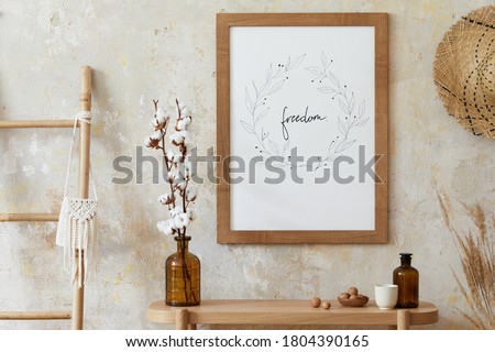 Beige boho interior of living room with mock up poster frame, elegant accessories, dried flowers in vase, wooden console and hanging rattan hut in stylish home decor. Template.