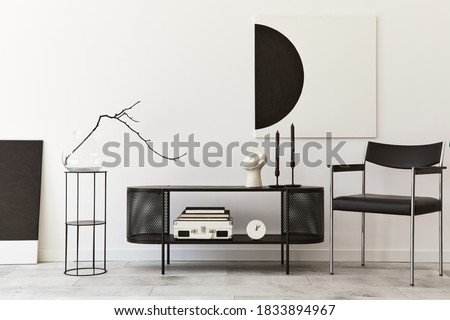 Interior design of modern living room with black stylish commode, chair, mock up art paintings, lamp, book, candlestick, decorations and elegant accessories in home decor. Template.