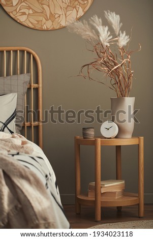 Cozy interior of stylish bedroom with design decoration, wooden bedside table, ceramic vessel, book, beautiful bed sheets, blanket ,pillows and personal accessories. Template.