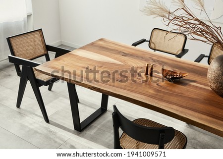 Interior design of stylish dining room interior with family wooden table, modern chairs, plate with nuts,  salt and pepper shakers. Concrete floor. White wall. Template.