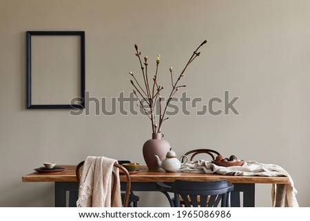 Stylish rustic interior of dining room with walnut wooden table, retro chairs, decoration, dried flower in vase and mock up picture frame in minimalist home decor. Template.