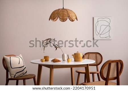 Boho and cozy space of dinning room with round family table, rattan chairs, design pedant lamp, carpet, decoration and personal accessories. Minimalist home decor. Template.	
 Imagine de stoc © 