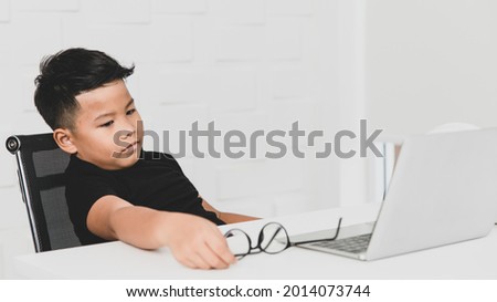 Poor young Asian boy on black shirt seriously sitting on chair near white working desk of laptop in home office, put glasses on table, and sadly facepalm as get stress and tired from difficult problem Foto stock © 