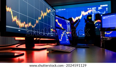 Close up shot of financial analysis graph chart stock exchange bitcoin cryptocurrency report on computer screen monitors and laptop on working in trading room while broker meeting in shadow behind.