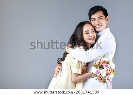 Portrait of young attractive Asian couple, man wearing white shirt, woman wearing beige dress hugging each other, woman holding bouquet of flower. Concept for pre wedding photography. Сток-фото © 
