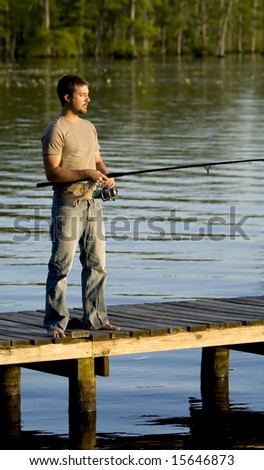 Man fishing on a dock in a bay as the sun in setting.