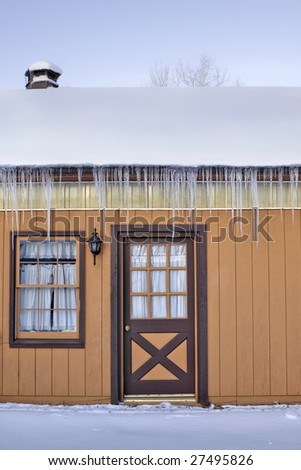 Long icicles hanging from the side of a home covered with snow.