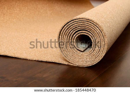 Roll of cork lies on a brown floor. The floor is made of pine and covered with semimatt lacquer
