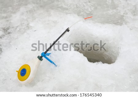 Colorful ice fishing rod standing at the edge of the hole.