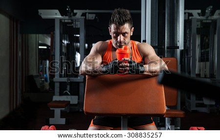the very muscular sporty guy drinking protein in dark weight room