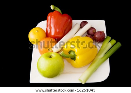 A plate of fresh fruits and vegetables on black background.