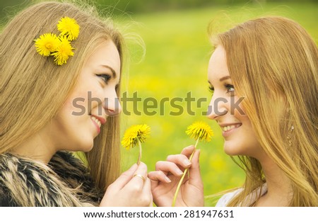 Two pretty girls with dandelions in the nature.
