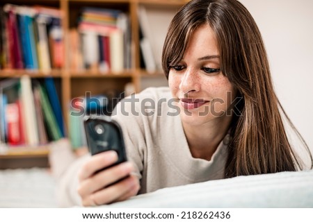 Woman using mobile phone while is lying on her bed.