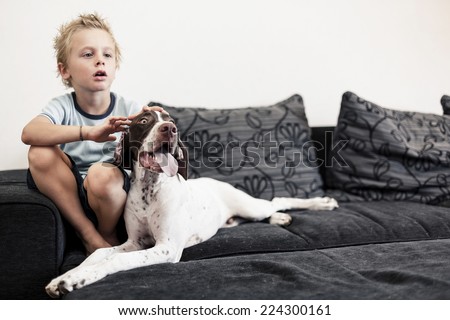 A young boy watching TV on the sofa with his big puppy.