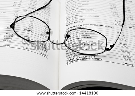 Modern thin reading glasses on open business book with balance sheet numbers