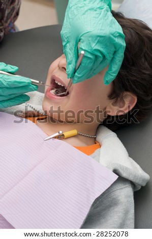 Young boy having his teeth checked at the dentist, doctor holding dental pick and mirror