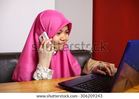 young muslim women speaking yo the phone while using laptop at her office