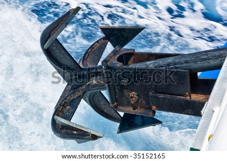 The big black shipboard anchor hanging down over the sea