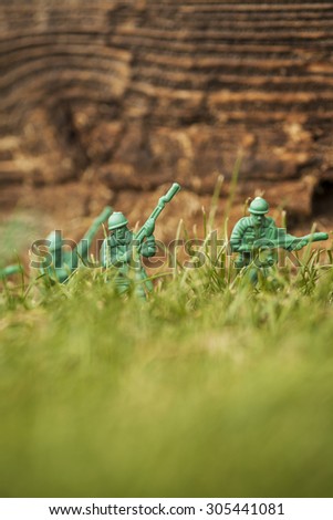 Green plastic toy soldier army unit walking through the overgrown grass. Selective focus and wooden textured background