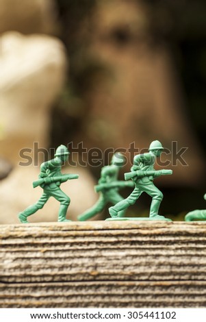 Green plastic toy soldier army unit running on top of an old weathered railway sleeper. Selective focus and wooden textured background