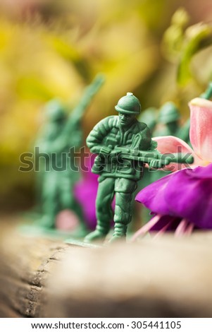 Green plastic toy soldier army unit walking on top of an old weathered railway sleeper. Selective focus, wooden textured background and purple flowers