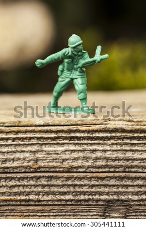 Green plastic toy army soldier throwing a grenade on top of an old weathered railway sleeper. Selective focus and wooden textured background