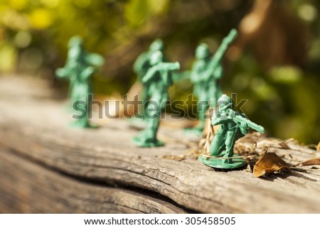 Green plastic toy soldier army unit walking on top of an old weathered railway sleeper. Selective focus, wooden textured background