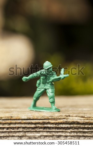 Green plastic toy soldier army unit throwing a grenade on top of an old weathered railway sleeper. Selective focus and wooden textured background