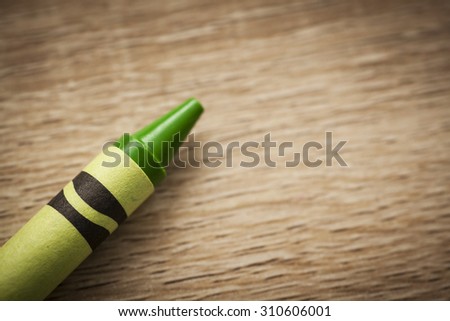 Individual green wax crayon on a wooden background with copy space to the right