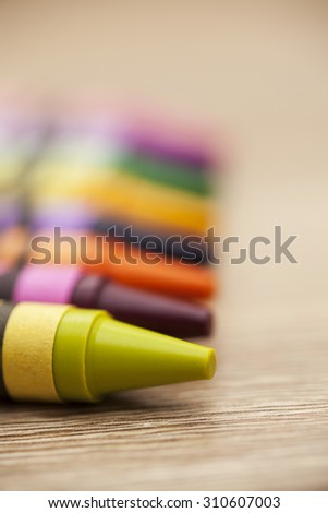Line of colourful wax crayons on a wooden background. Lime green crayon at the front. Copy space to the right