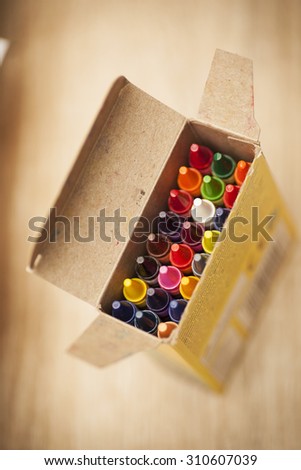 Open box of 24 colourful wax crayons on a wooden background