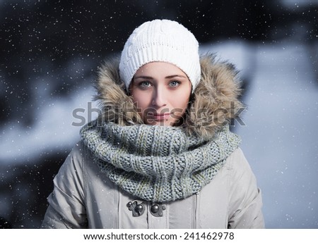 Face close up of beautiful happy young woman wearing winter gloves covered with snow flakes. Christmas snowing portrait concept.