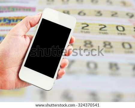Female hand holding mobile smart phone on Thai lottery tickets blur background, business concept