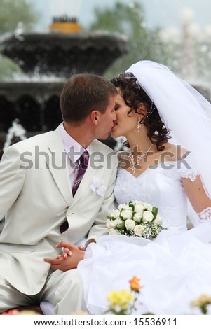 The groom and the bride near a fountain kiss
