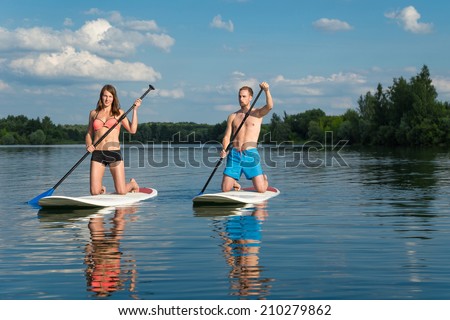 Young attractive couple knees on stand up paddle board in the lake, SUP