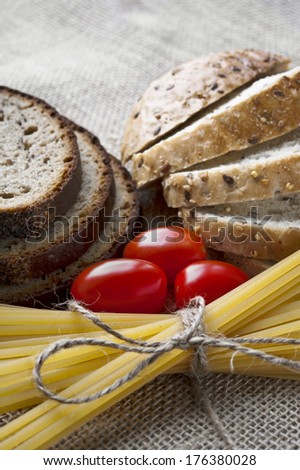 Dry pasta and tomatoes, sliced bread with seeds on sack background. Closeup.
