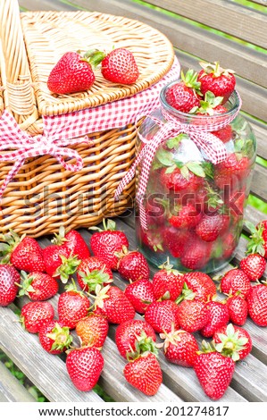 Many fresh ripe strawberry in basket and glass jar on wooden background. Bounty summer crop in garden. Outdoors.