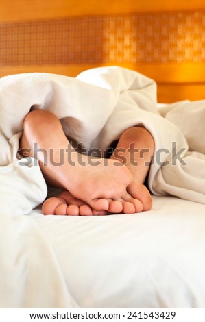 Sleeping child dirty feet on white bed linen from backside. Indoor.